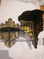Two black wooden chinoiserie picture shelves with gilded hand-painted Japanese scenes, shown from top view displaying surface and bracket design.