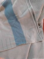 Close-up showing the blue broad stripe pattern on a light beige wool fabric with finished sewn edges.