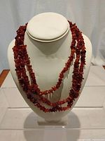 Necklace displayed on a white bust stand showing chunky red amber beads.