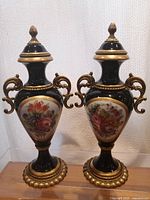 Front and side view of pair of black urn-shaped vases with gilt ormolu mounts and colorful hand-painted floral oval.