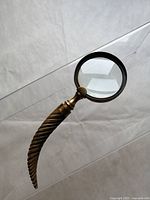 Full view of antique magnifying glass showing twisted horn handle and brass frame around clear glass lens.
