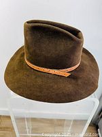 Brown suede cowboy hat with leather band on crown, viewed from the side.