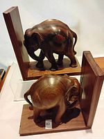 Front and side view of the carved teak elephant bookends showing natural wood grain, white stone eyes, and size relative to surroundings.
