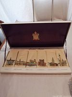 Open display box showing six embroidered linen napkins aligned with their respective London scenes embroidered and labeled underneath.