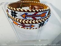 Close-up photo showing detailed handmade beadwork on leather belt with arrow and geometric bead motifs and leather thong edge stitching.