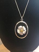 Close up of the floral sterling silver pendant with yellow rhinestone center against black background.