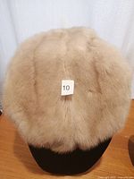 Top view of a round, beige mink fur hat on a black display bust, showing the full fur texture.