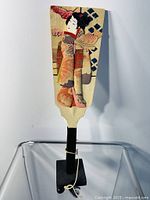 Full front view of the wooden paddle showing the Geisha in patterned silk kimono with black handle.
