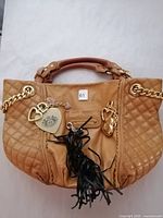 Front view of tan Juicy Couture leather handbag with visible gold-tone heart charms and black leather tassel attached to handle