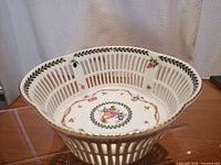 Angled side view showing reticulated porcelain lattice sides, hand painted fruit and floral motifs inside and gold trim on the rim