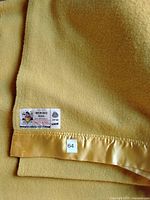 Close up of the blanket showing the satin trimmed edge and Marquise label indicating 100% merino wool and made in England.