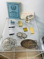 Photo showing mixed collectible lighters, coins, belt buckles, blue handbook, and booklet.