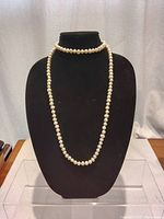 Front view of the pearl necklace hanging long on black display stand showing lustrous round pearls.