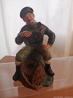 Front view of the Royal Doulton figurine showing the seated fisherman holding the lobster with the lobster creel beside him.