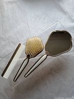 Photo showing the hand mirror, removable hairbrush, and white comb on a clear surface from a top-down view.