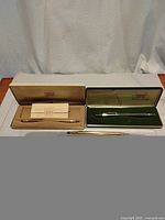 Three vintage Cross pens with two cases, one green velvet and one cream colored, displayed and photographed on a table with a white backdrop.
