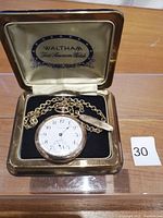 Open presentation box with watch, chain, and tie clip displayed on black velvet insert