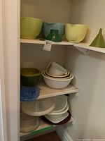 Plastic mixing bowls in pastel green and white, plastic funnels, strainers, and bowls stacked on shelves.