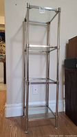 Front angle view of the four-tier chrome and glass shelf unit showing construction and condition.