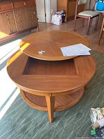 Round wooden coffee table with pivoting top layer revealing storage below and round bottom shelf