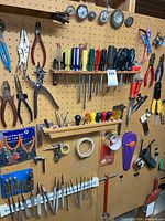 Wide view of pegboard showing various screwdrivers, pliers, punch, tape and other hand tools hung and arranged on hooks.