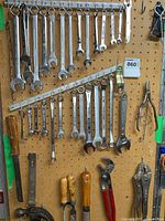 Photo of multiple combination and open-end wrenches hanging on pegboard along with some hand tools such as wrenches, putty scrapers, and pliers.