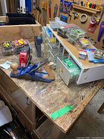 Blue hand planer on workbench with wood drawer organizer containing hardware items and stapler tool, loose boxes of staples.