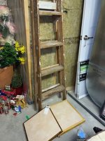 Five-foot wood step ladder standing in basement near furnace room, showing worn paint spots and wood material.