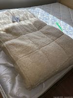 Full view of folded cream-colored wool mattress cover placed on a white mattress showing plush quilted texture.