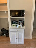 Front view of the white microwave stand with microwave and cookware on top and inside the open shelf.