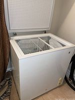 White GE brand mini chest freezer with top lid open showing internal storage basket.