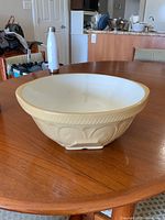 Large ceramic mixing bowl with cream-colored embossed exterior and white glazed interior, placed on wooden table.