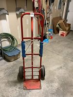 Front view of red metal movers dolly standing upright on garage floor, showing foam-padded handles and platform base.