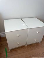 Photo of two white night tables side by side, showing clean flat tops and two drawers each.