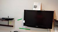 Panasonic TV mounted on wall with manual placed behind on top edge of TV.