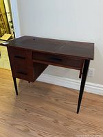 Front angle view of the solid wood retro desk showing three drawers and tapered black legs.