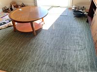 Overall view of the green area rug under a wooden round coffee table with white wave pattern design.