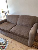 Overall view of the brown fabric sofa bed positioned against a white wall on a patterned carpet.