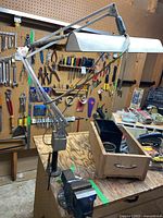 Blue industrial table lamp with adjustable arm mounted on wooden surface next to vice.