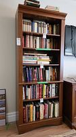 Front view of six-tier wood bookshelf filled with books, showing overall design and condition.