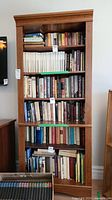 Front view of bookshelf filled with books, showing six shelves and wood finish.