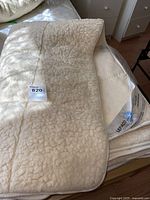 Top view of cream-colored wool mattress cover showing textured wool surface and label with lot tag attached.