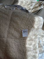 Mattress cover folded, showing soft textured cream wool surface and part of fabric edge with securing strap.