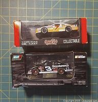 Two 1/43 diecast NASCAR model cars in their original boxes: Revell Dale Earnhardt Oreo/Goodwrench Monte Carlo and Quartzo Alan Kulwicki number 7.
