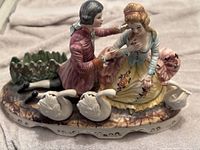 Porcelain Baroque-style couple figurine seated with three swans on decorative base.