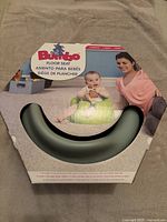 Front view of boxed Bumbo floor seat showing green seat and package with baby and mother on it.