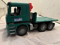 Side view of the green Bruder truck with flatbed, showing 6 wheels, open cab with black seats, Bruder logo and numbering on door