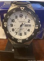 Front view of Casio Men's Diver Style Quartz Watch showing silver dial with black Arabic numerals, black rotating resin bezel, day-date display, and stainless steel strap.