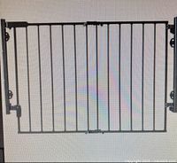 Gray metal safety gate with vertical bars and mounting hardware visible on sides. Appears fully assembled and ready to install.
