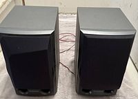 Front view of two grey-black Pioneer bookshelf speakers side by side with cables at the back, showing fabric grille and front bass ports.